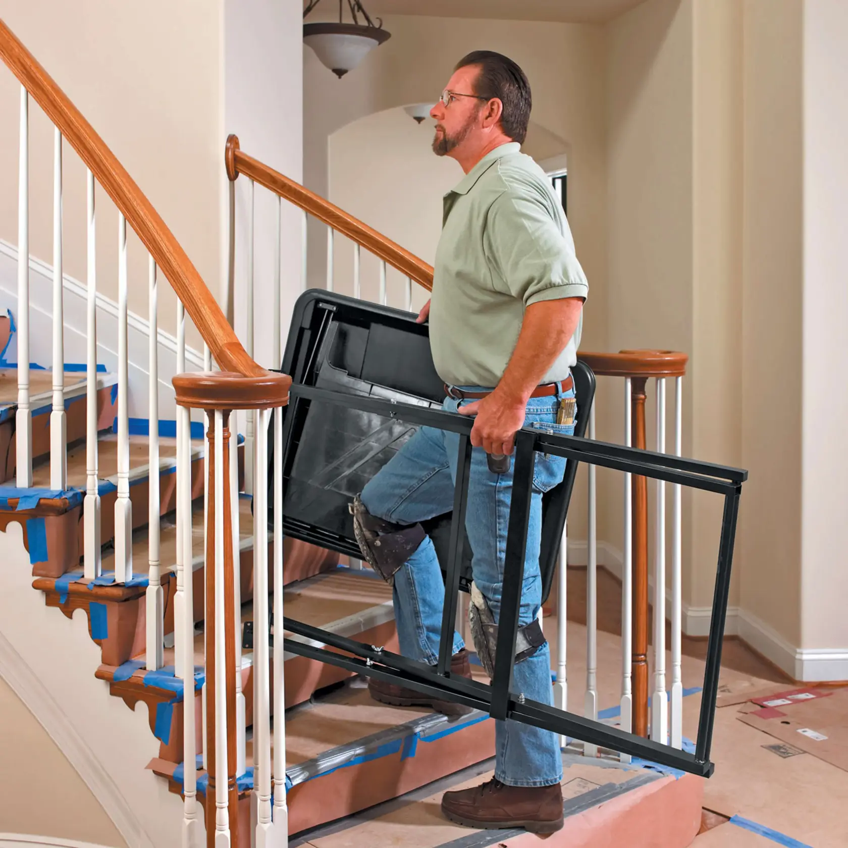 Person carrying DEWALT D24000 tile saw stand frame up a staircase with protective coverings on the steps.