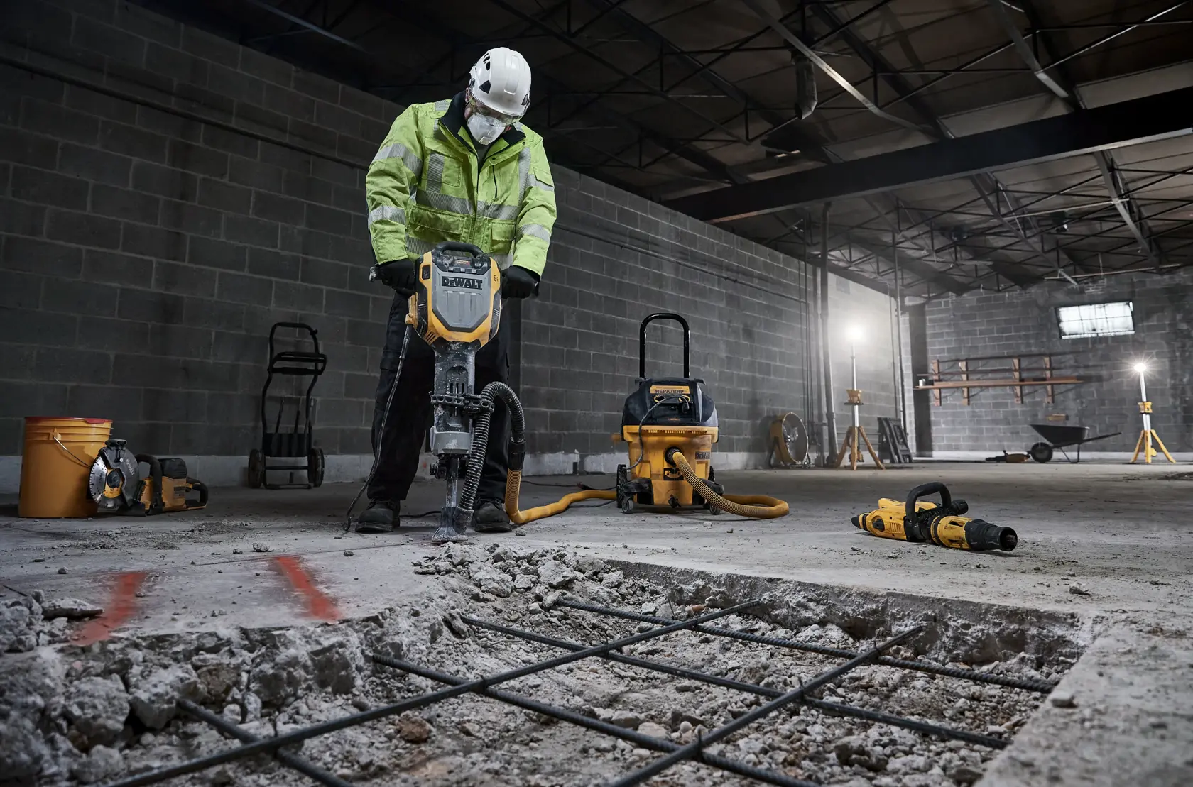 Worker uses DEWALT D25966, D25966-B2 breaker on concrete in warehouse. Construction tools are visible.