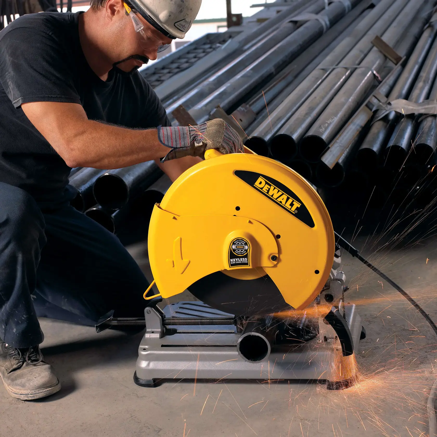 A worker using a DEWALT D28715 yellow metal chop saw to cut a steel pipe, with sparks flying, in an industrial setting with stacked pipes in the background.