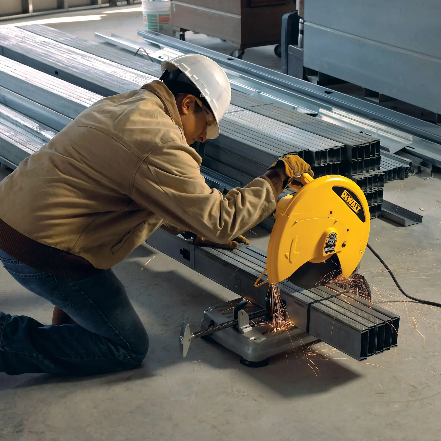 A person wearing safety gear uses a DEWALT metal cutting saw to cut steel pipes in an industrial setting. Sparks are visible as the saw is in operation.