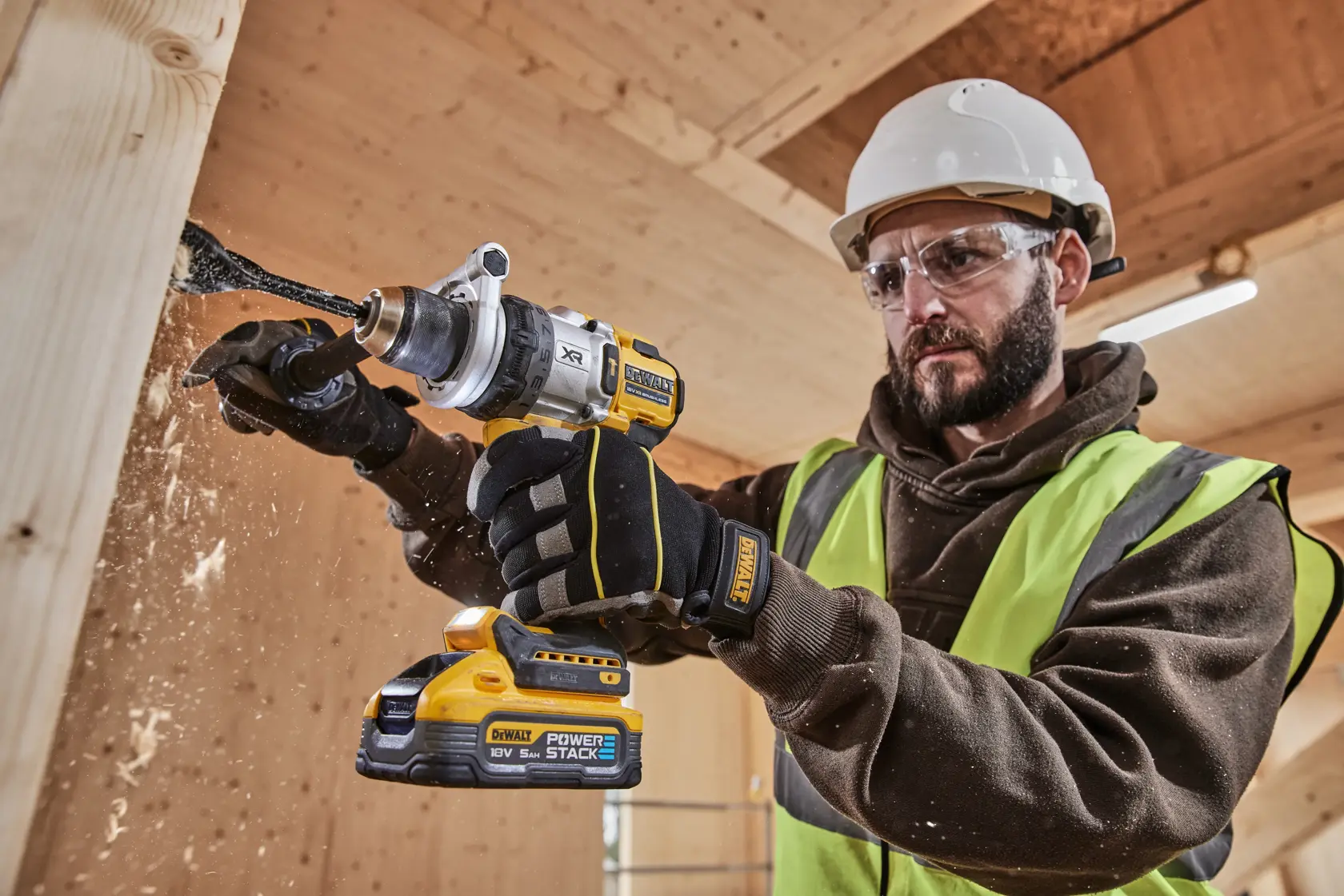 DEWALT cordless drill in use on wood, worker wearing gloves, helmet, and hi-vis vest in construction setting.