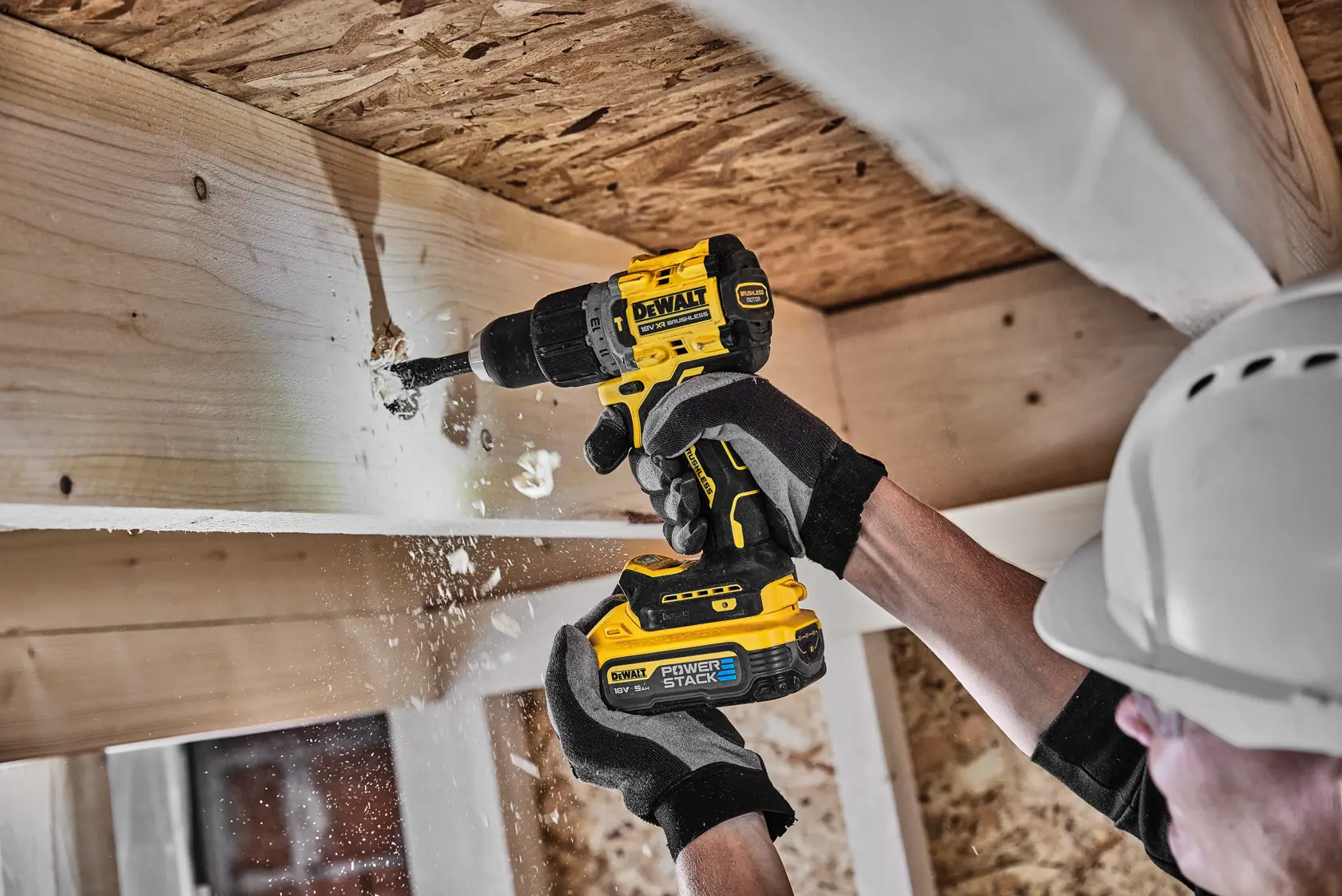 Person uses DEWALT cordless drill to make a hole in wooden beam, wearing gloves and hard hat.