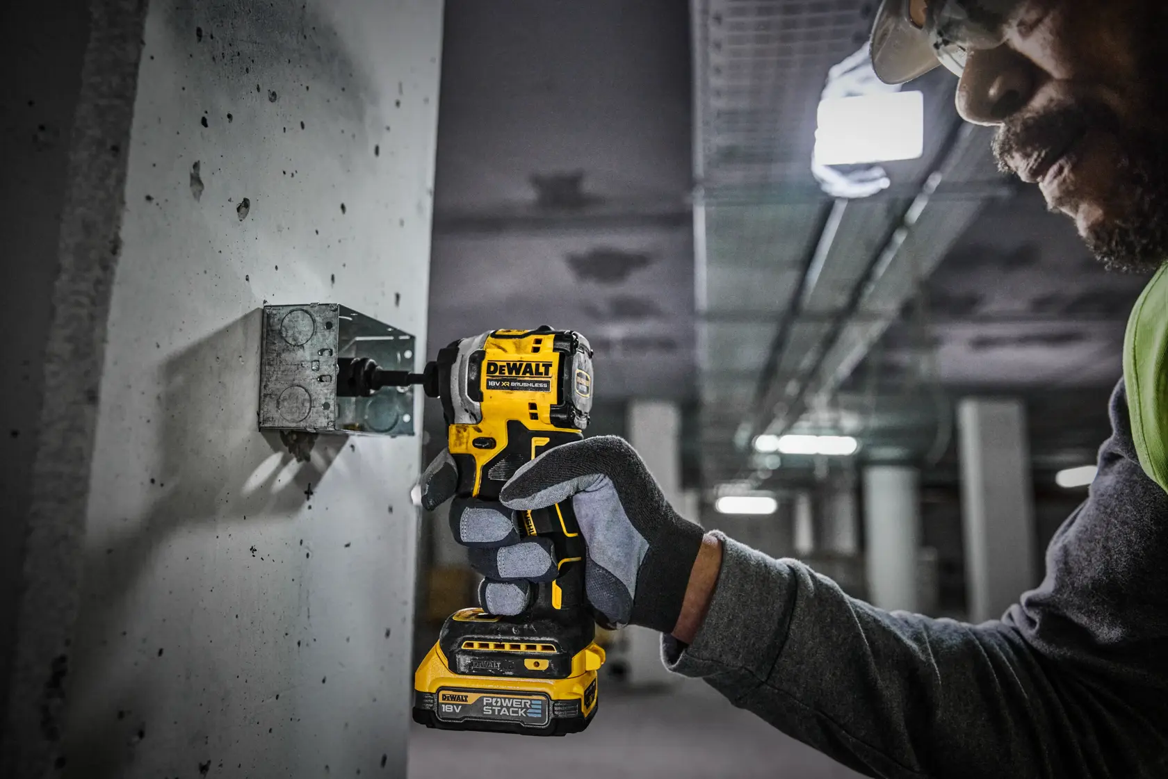 A person wearing gloves and safety gear is using a DEWALT DCF850E2T cordless impact driver to secure a metal bracket to a