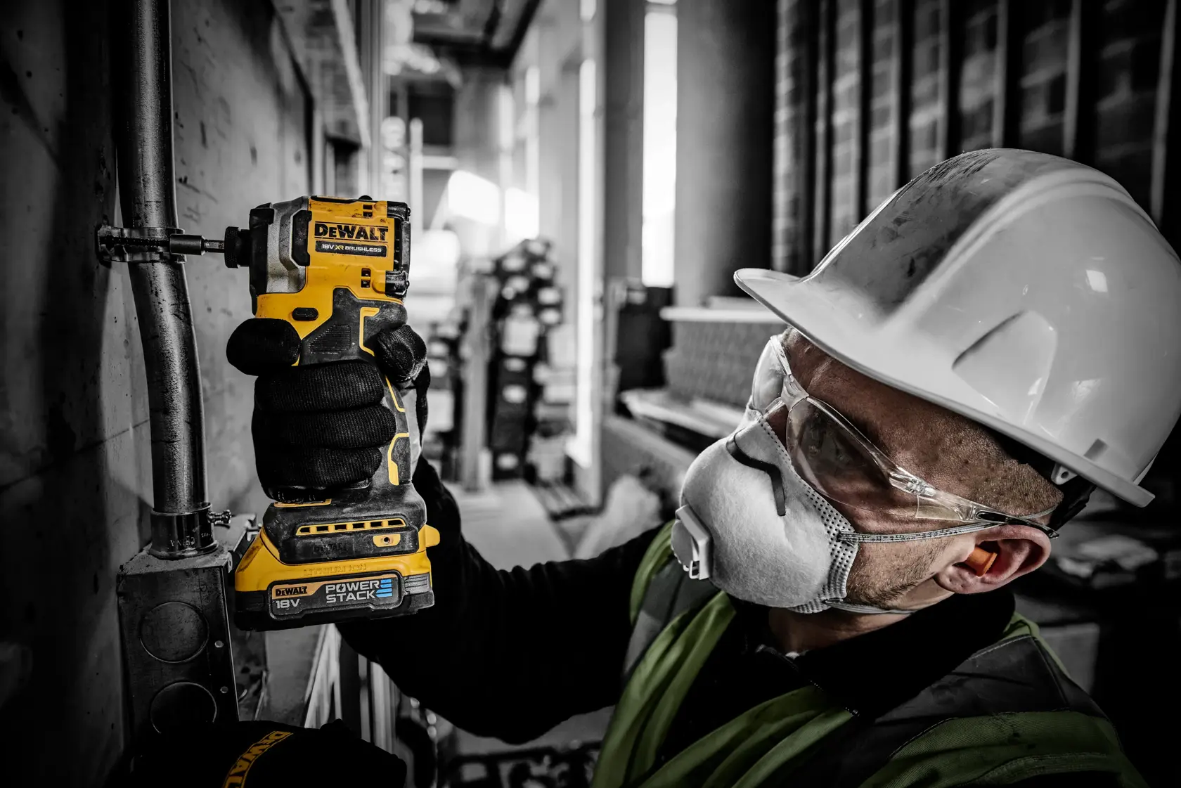 Worker uses DEWALT DCF850E2T cordless drill on metal pipe, wearing safety gear and helmet at a construction site.