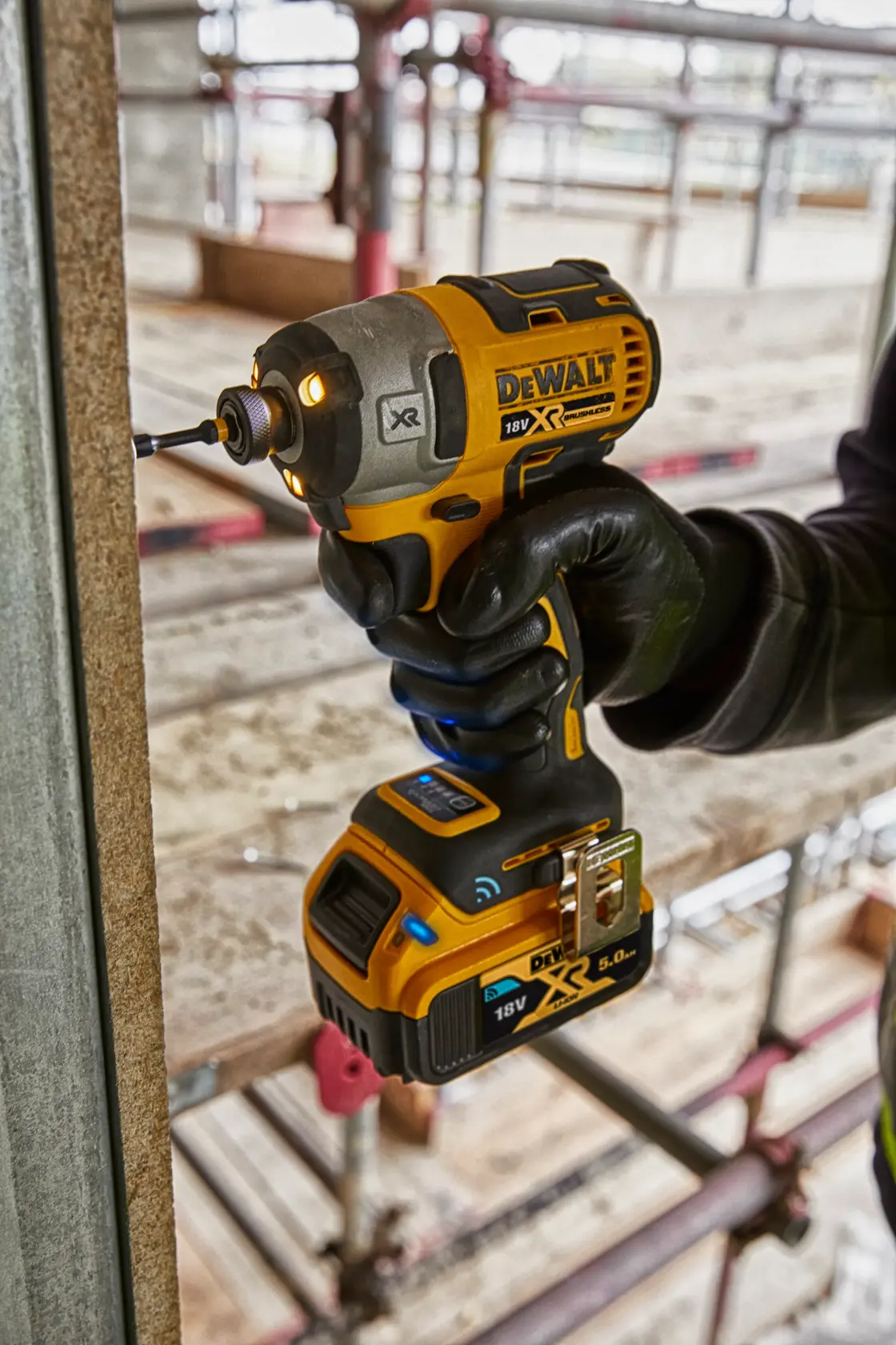 DEWALT cordless impact driver DCF888D2B in use on a construction site, held by a gloved hand.