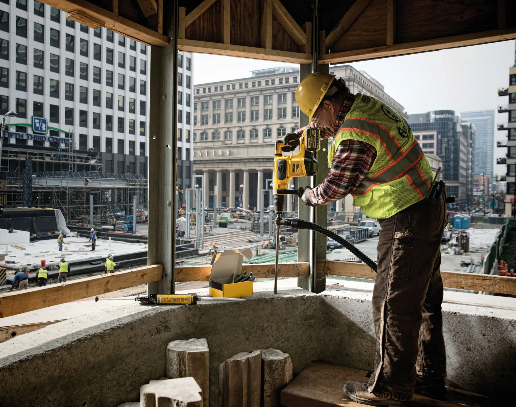 DEWALT drill DCH481X2, DCH481X2-GB used by worker on urban site. Concrete, cityscape visible. SKU: DCH481X2, DCH481X2-GB.