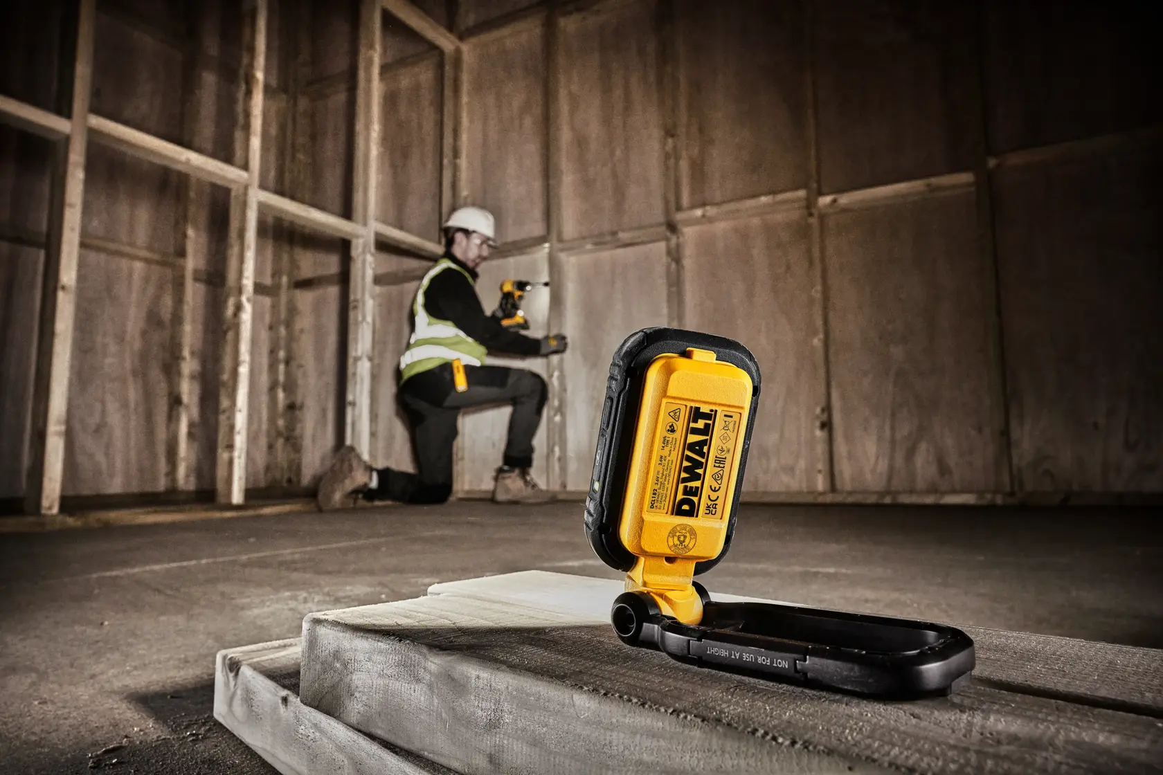 Lampe de travail LED portable DEWALT DCL182 avec un boîtier robuste noir et jaune, un support réglable et plusieurs ampoules LED, présentée sur fond blanc.