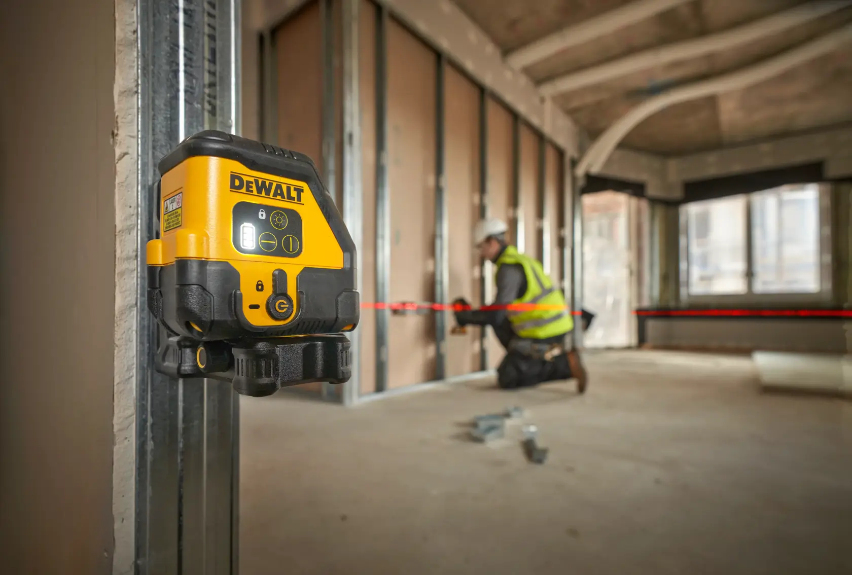 DEWALT laser level attached to metal framing. Worker in background aligns materials using red laser line.