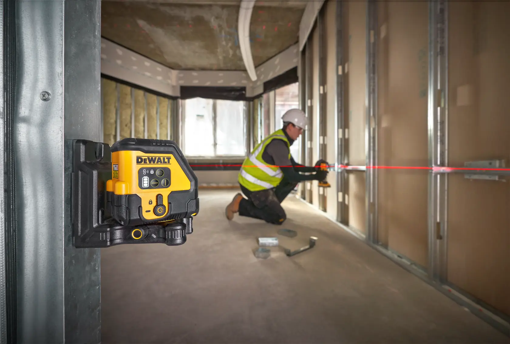 DEWALT laser level mounted in construction, worker aligns metal framework using red laser line.