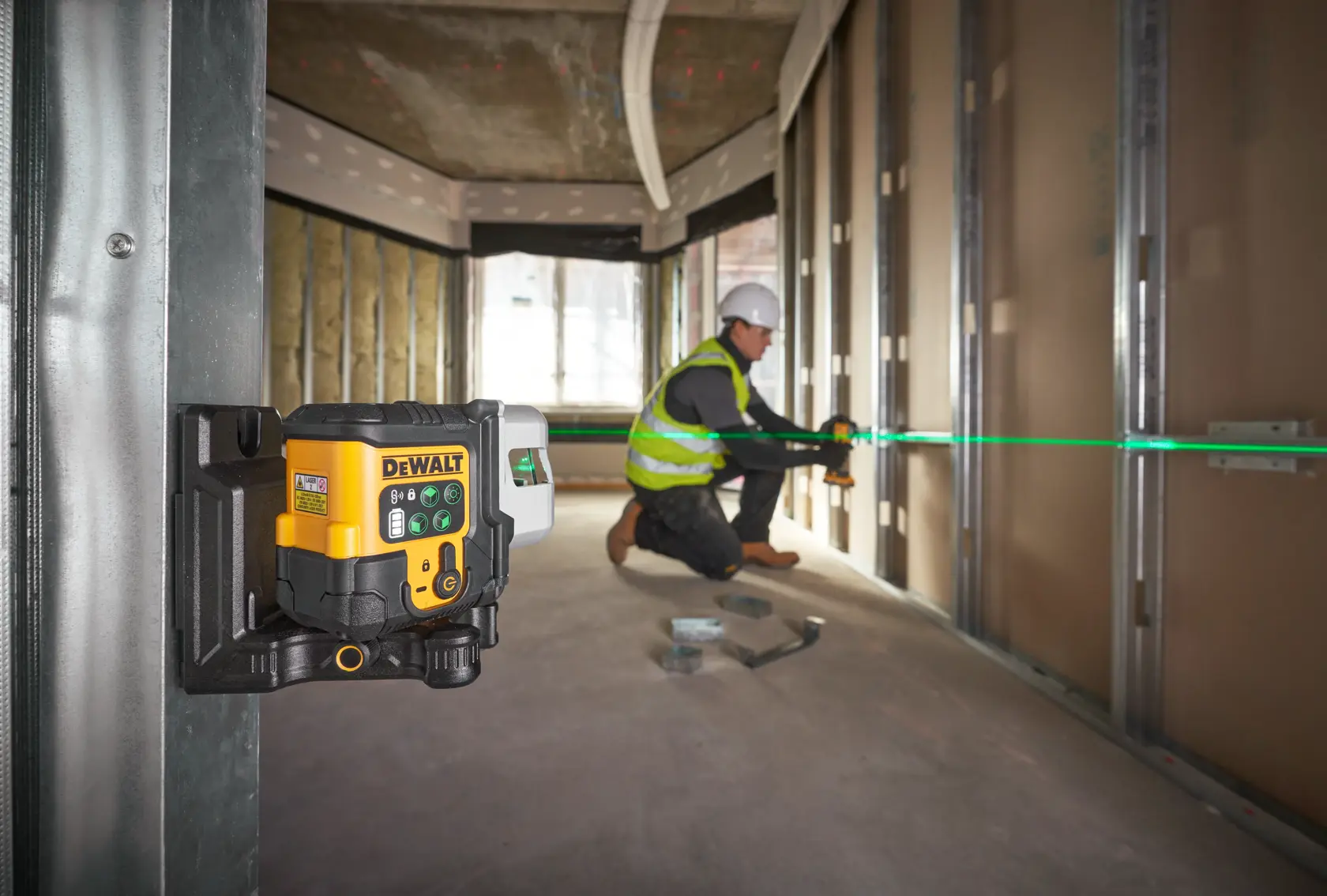 DEWALT laser level projecting a green line, used by a worker for wall alignment on a construction site.