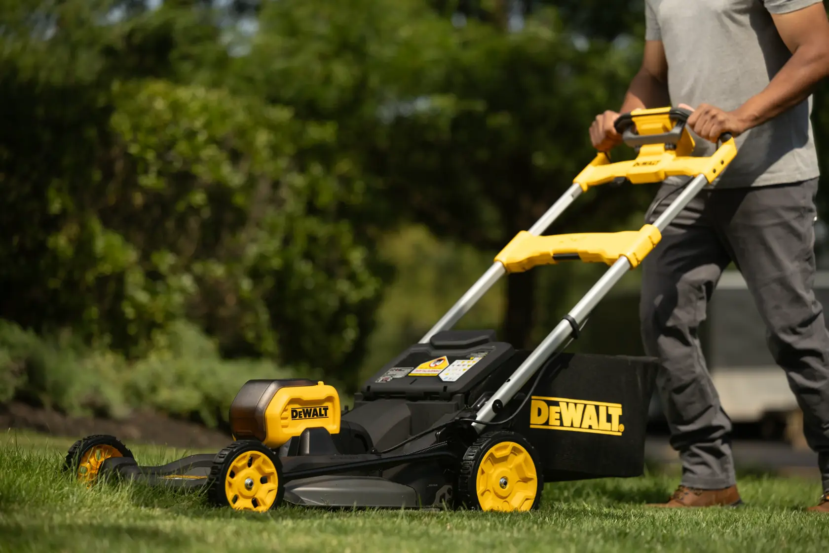 Persona usando cortacésped inalámbrico DEWALT sobre césped verde, vista cercana del mango y el cortacésped.