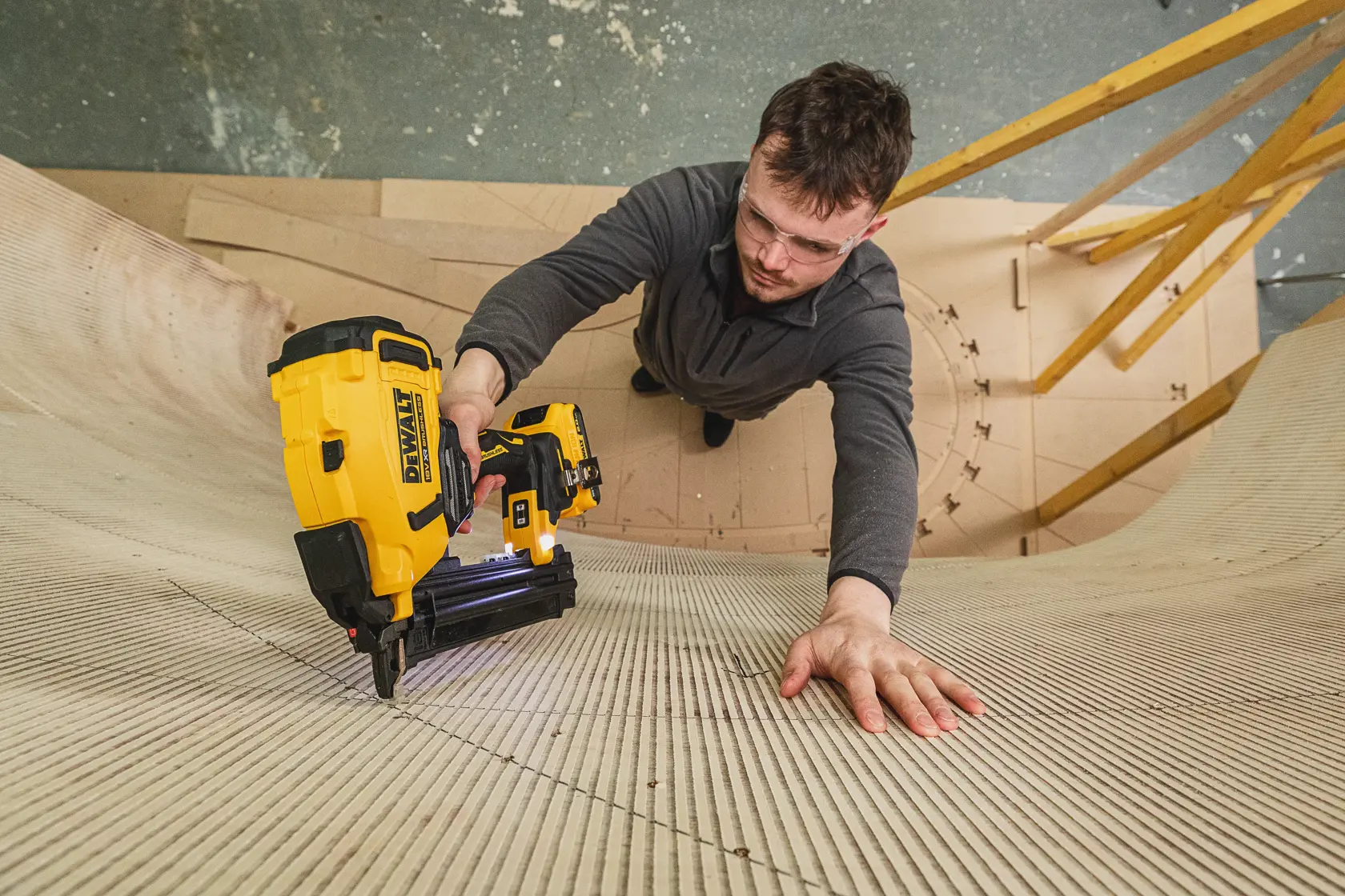 Person using a DEWALT DCN210SN-XJ nailer to fasten curved wood panels in a workshop setting.