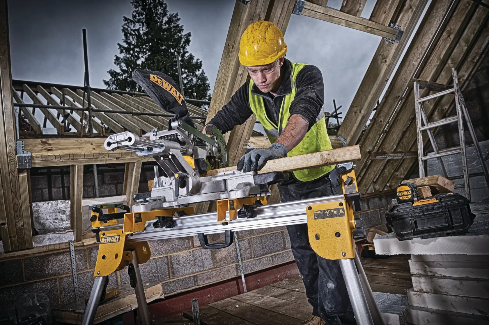 Worker cutting wood with DEWALT DCS365M2 saw at construction site, wearing safety gear and hard hat.