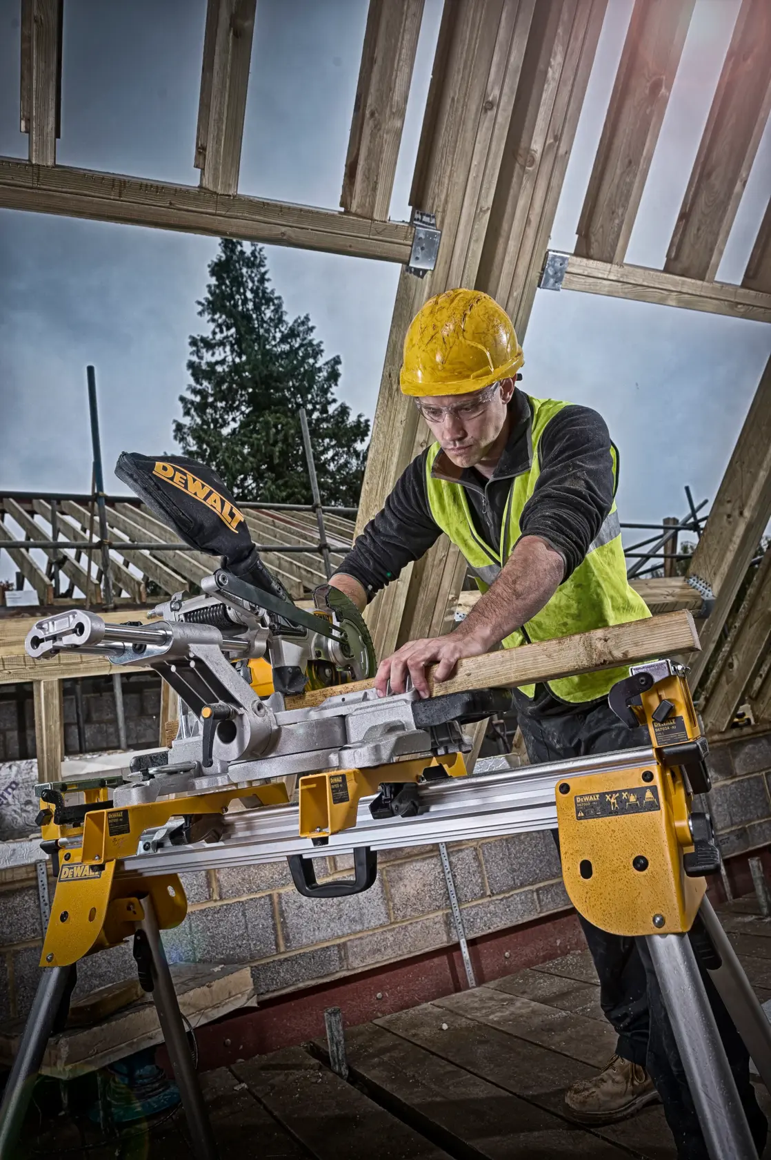 Worker uses DEWALT DCS365M2 saw to cut wood at a construction site. Wearing yellow hard hat and vest.