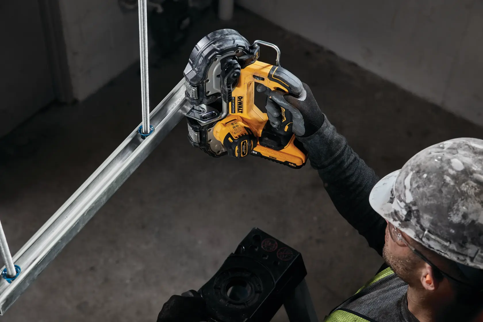 Worker uses yellow DEWALT cordless bandsaw to cut metal pipe in industrial setting.