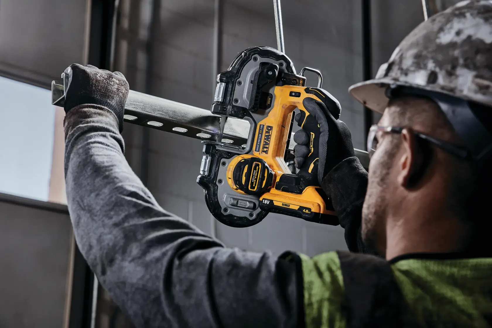 Person using a DEWALT cordless band saw to cut a metal pipe indoors, wearing gloves and a helmet.
