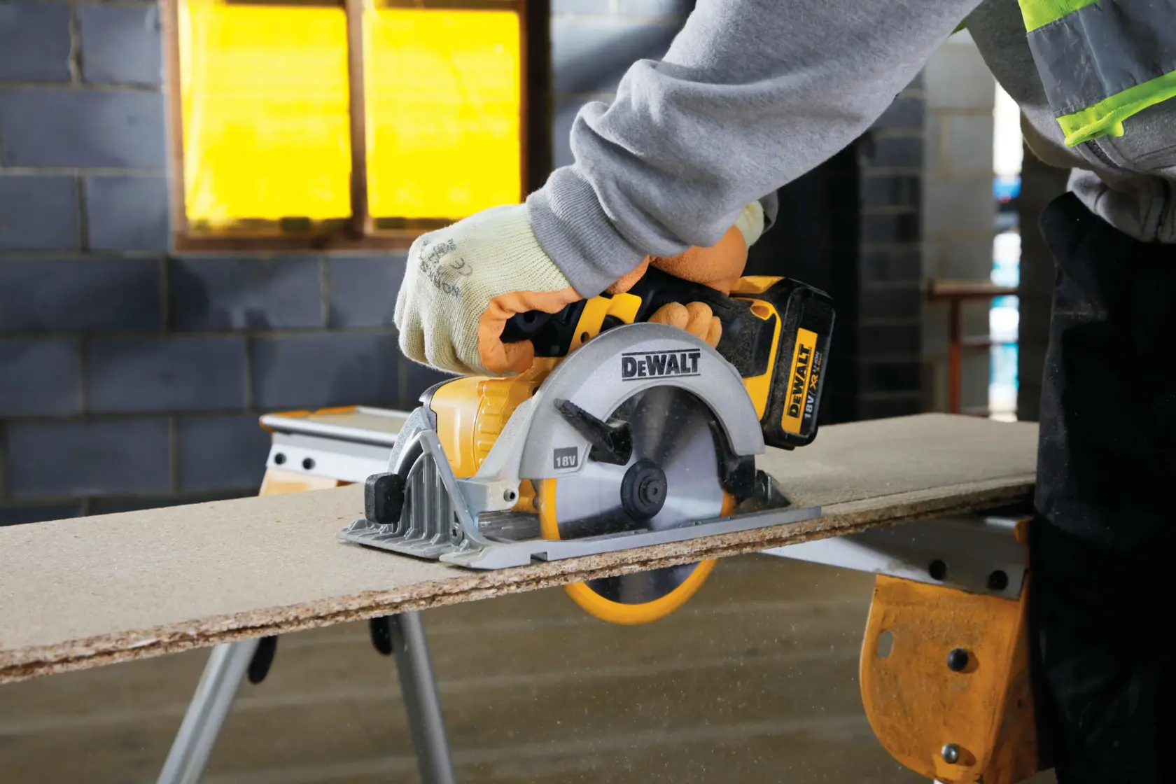 Person using DEWALT cordless circular saw to cut wood panel on workbench in workshop.