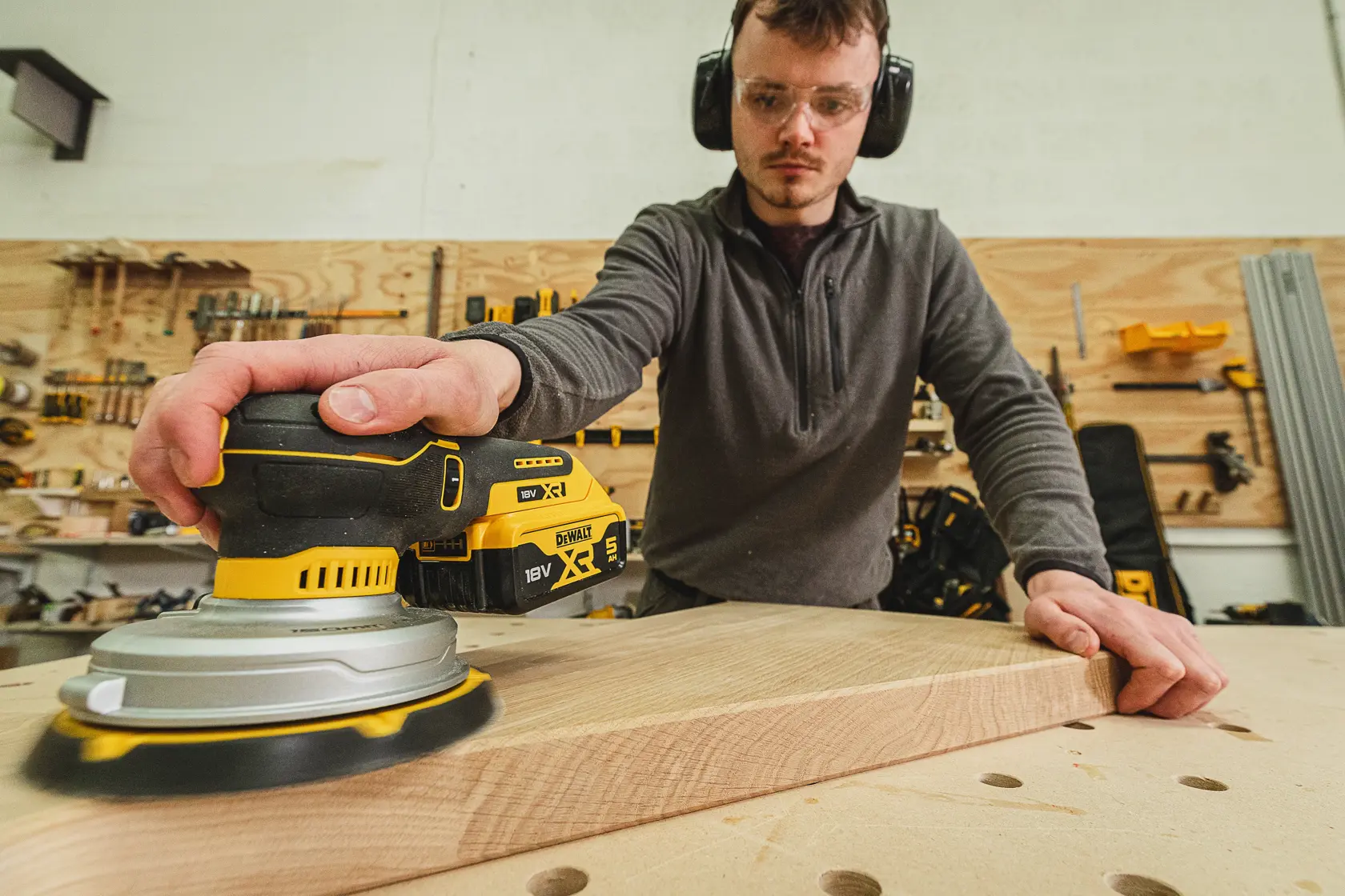 Person sanding wood using a DEWALT DCW230N-XJ cordless sander in a workshop.