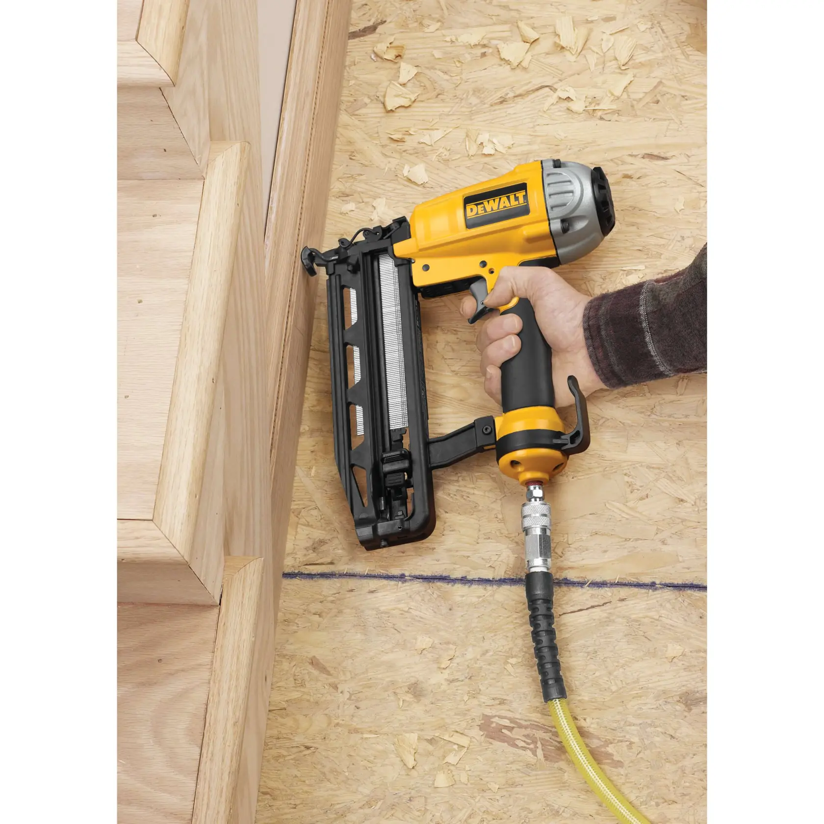 DEWALT DPN1664 nail gun in use, fastening wood on a construction site with a hose attached.