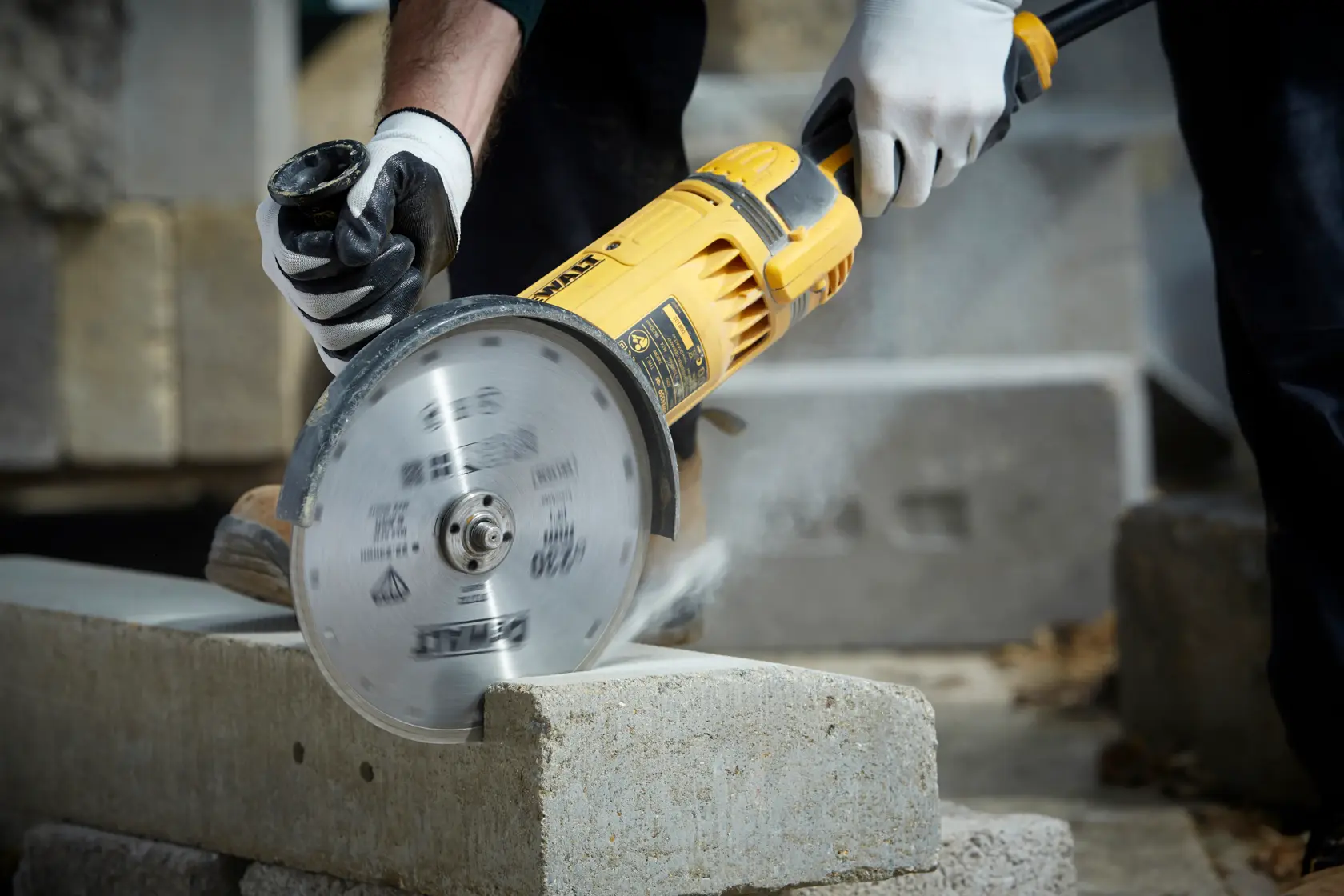 DEWALT cutting tool in use, slicing concrete block. Worker wears gloves for safety.