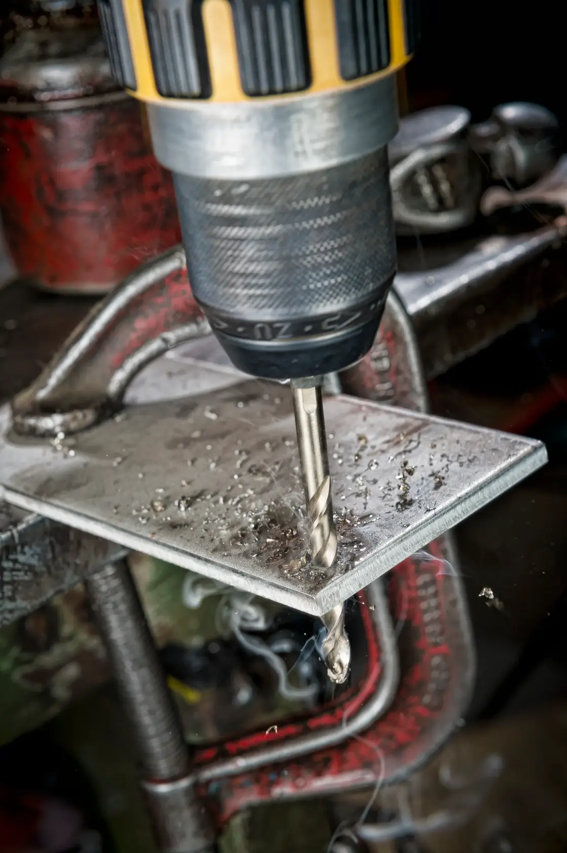 Close-up of a drill making a hole in a metal plate held in place by a clamp.