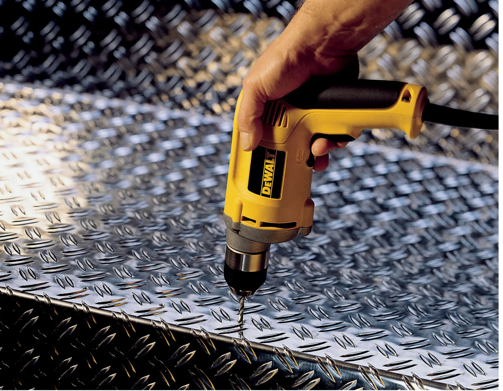 A DEWALT drill being used to drill into a metal plate with a textured surface.