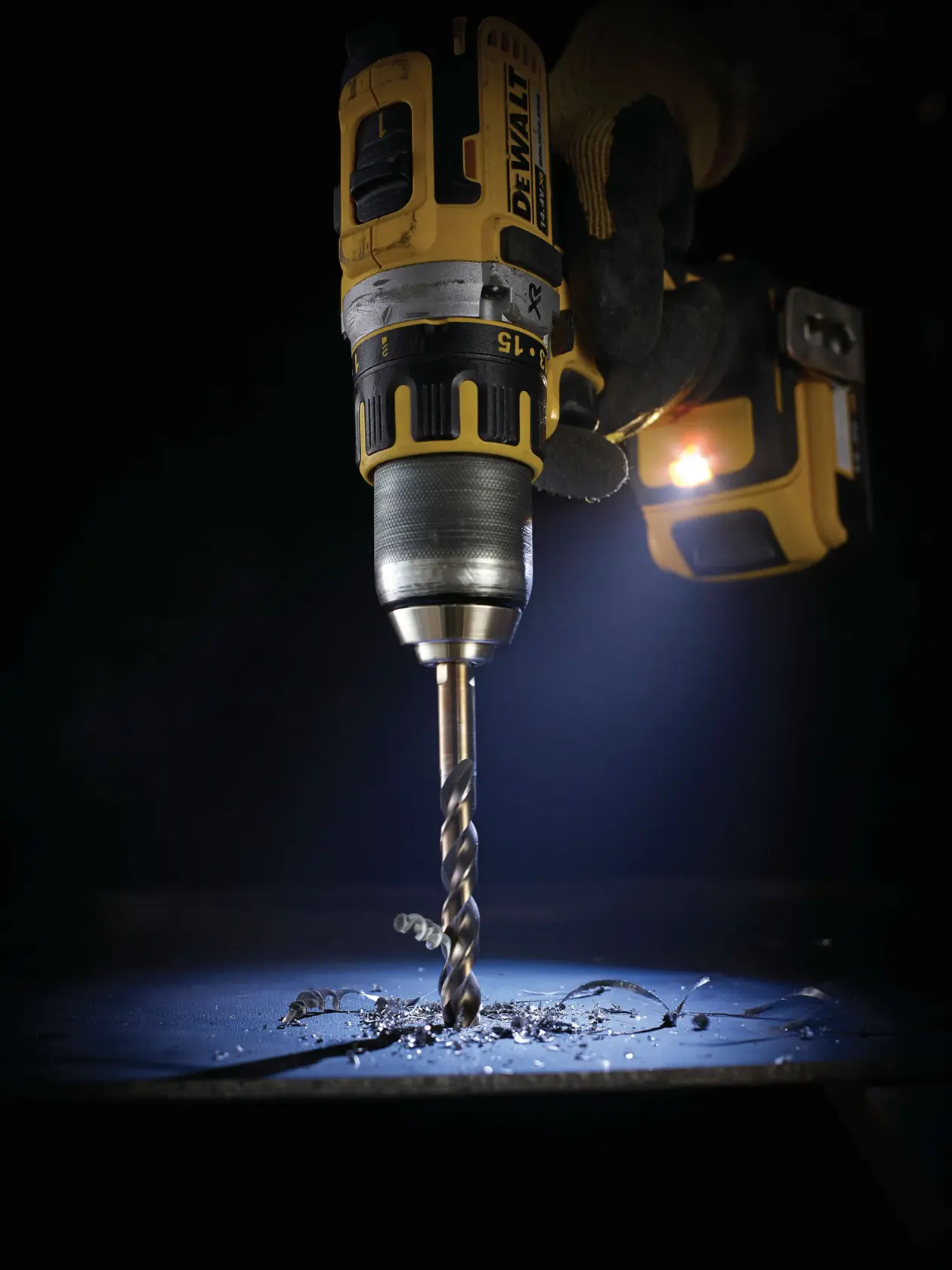 Taladro inalámbrico DEWALT perfora metal, virutas dispersas bajo luz focalizada.