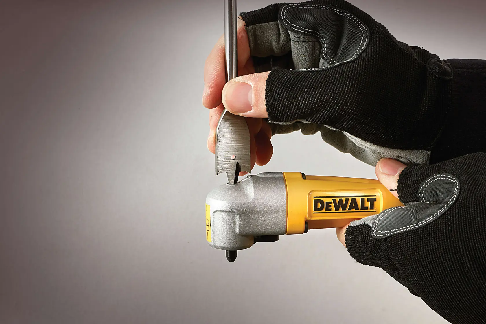 Gloved hands use a DEWALT right angle attachment with a drill bit, close-up on tool and hands.