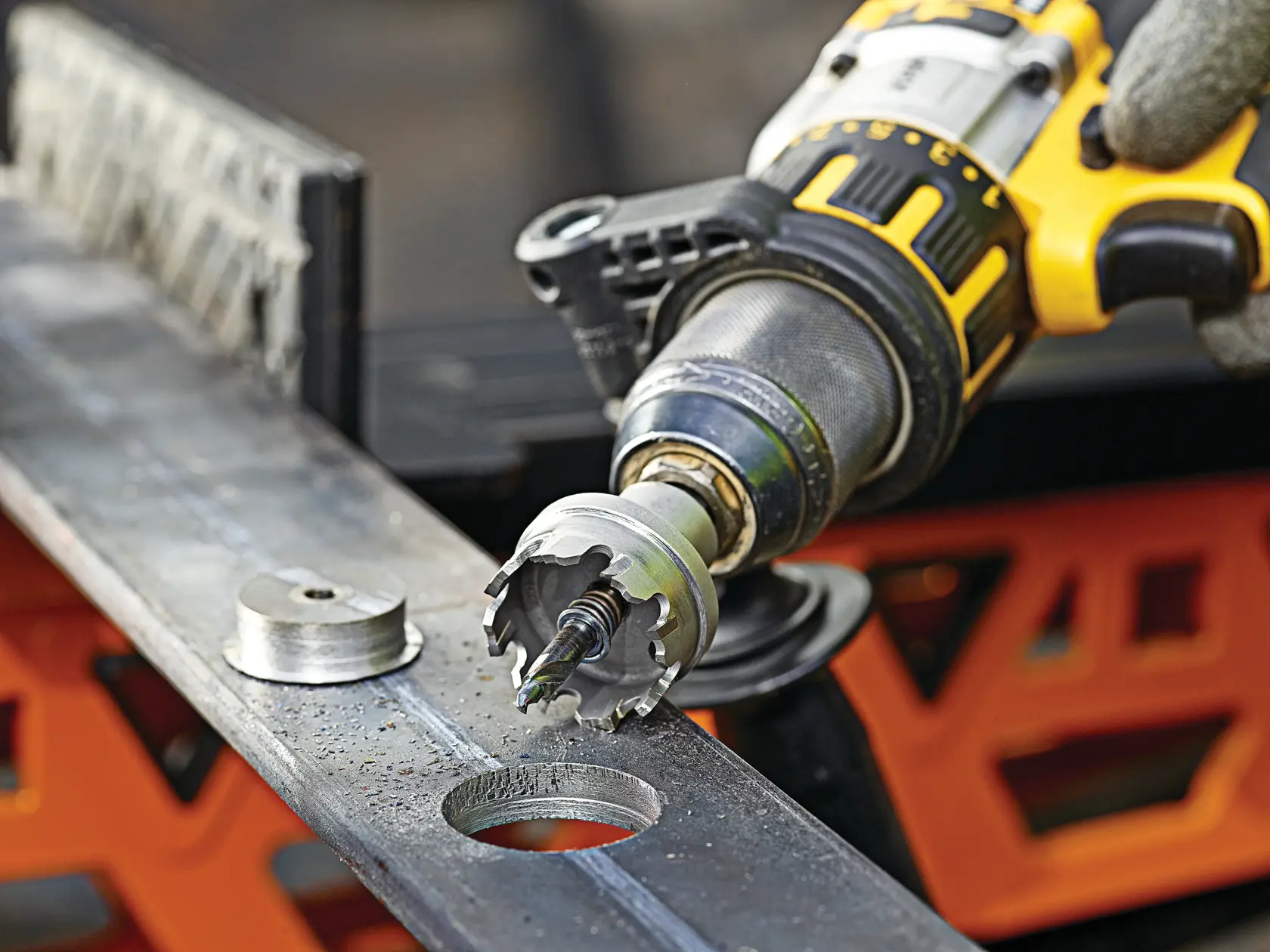 DEWALT drill with hole saw bit cutting a circular hole in metal, disc removed, close-up view.