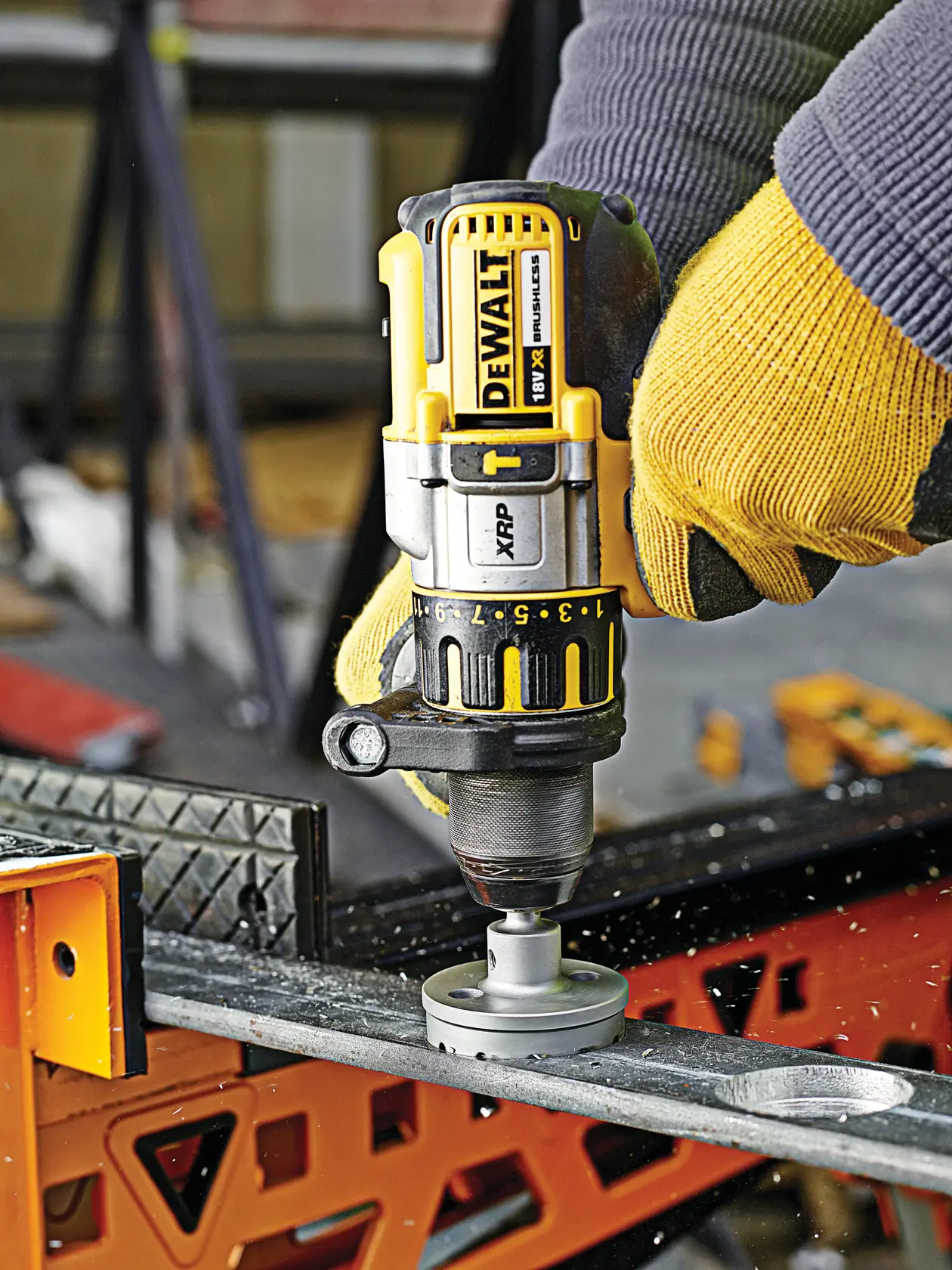 DEWALT drill in use, operator with gloves drilling a hole through metal on a workbench, close-up workspace scene.