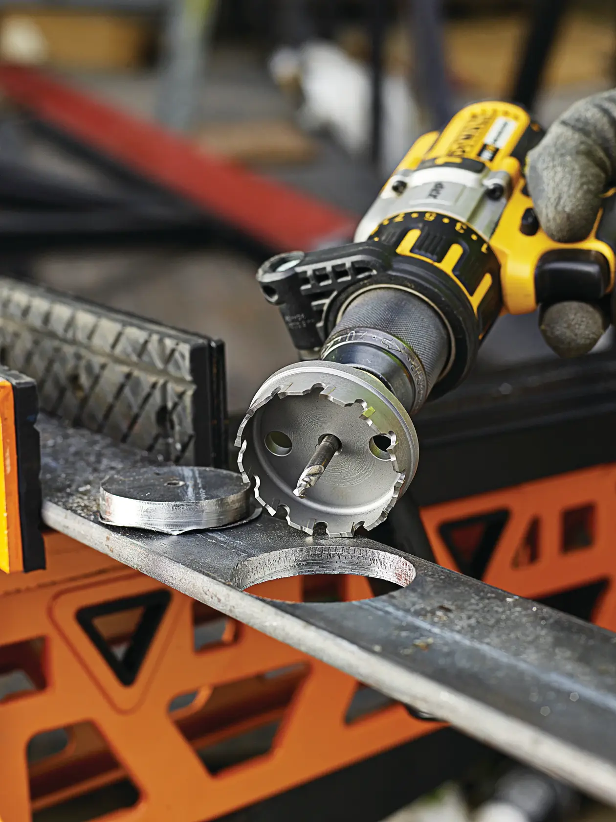 DEWALT drill with DT8353 hole saw cutting a metal sheet, showing the cut-out circle and tool in use.