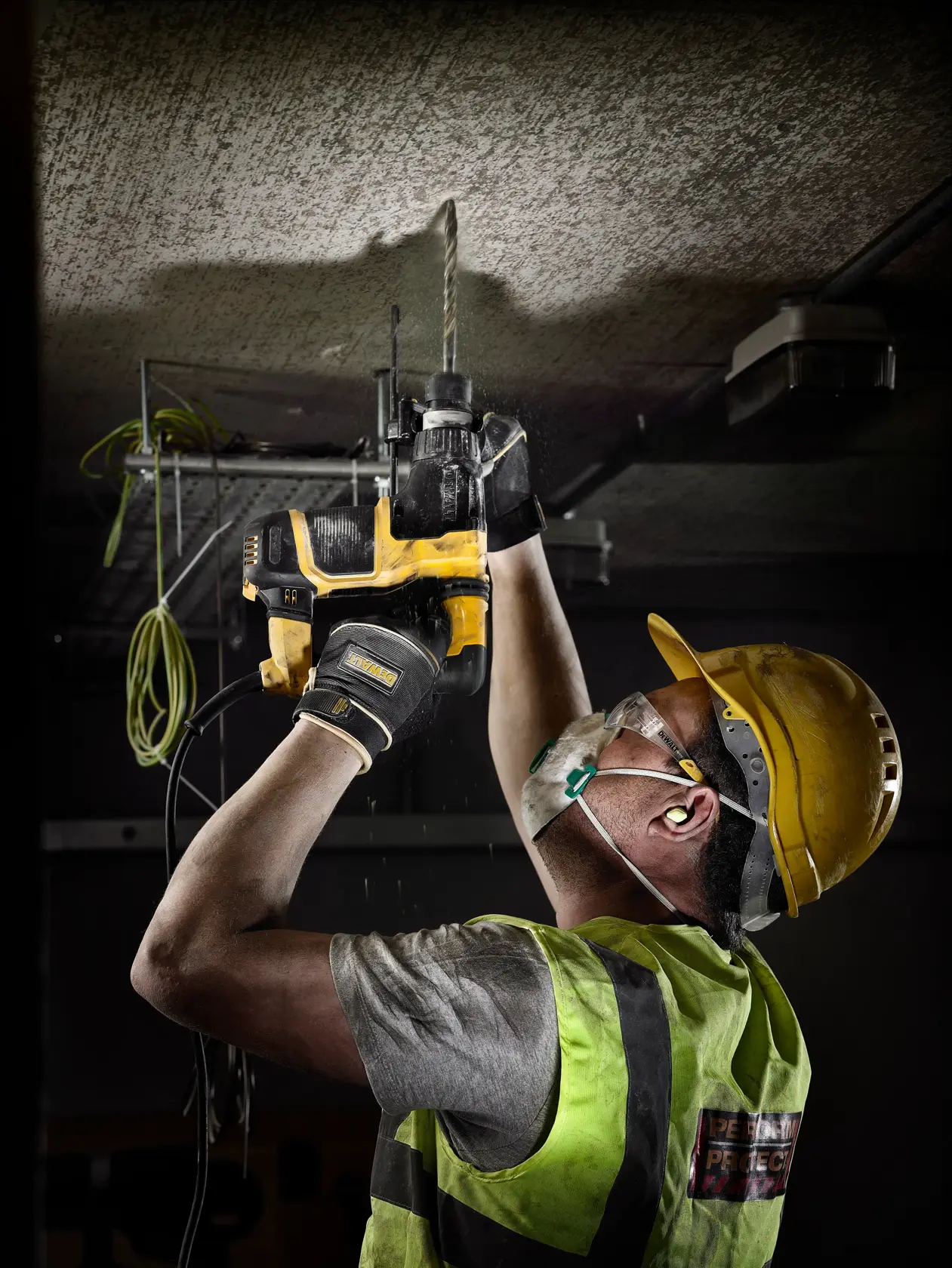 Trabajador equipado usa taladro Dewalt para perforar el techo en una obra.