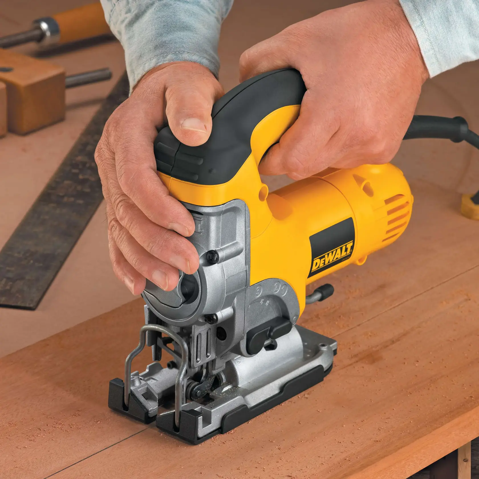 Hands operating a yellow DEWALT electric jigsaw on a dark sheet of material, cutting along an edge.