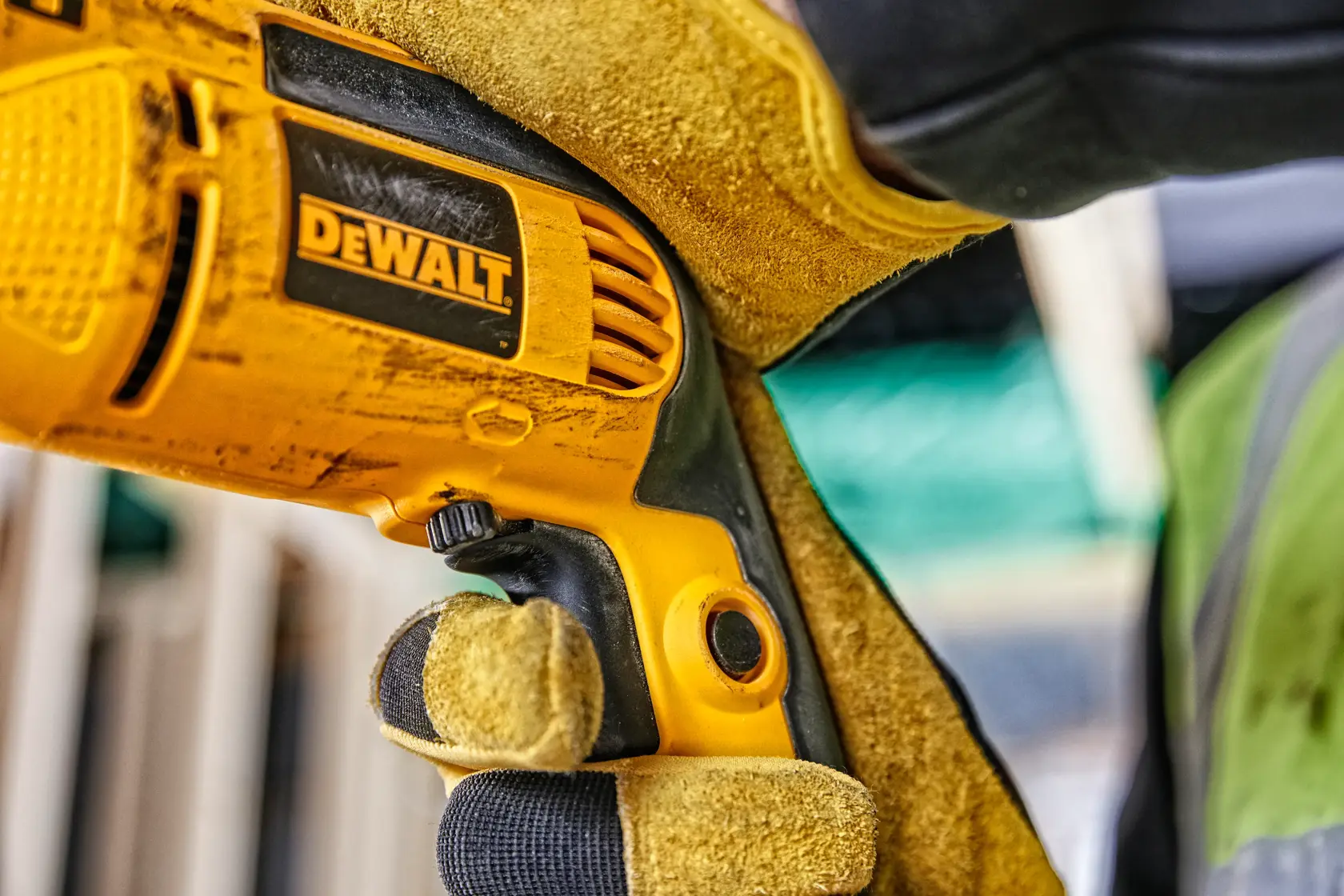 Close-up of a gloved hand holding a DEWALT electric drill at a construction site.