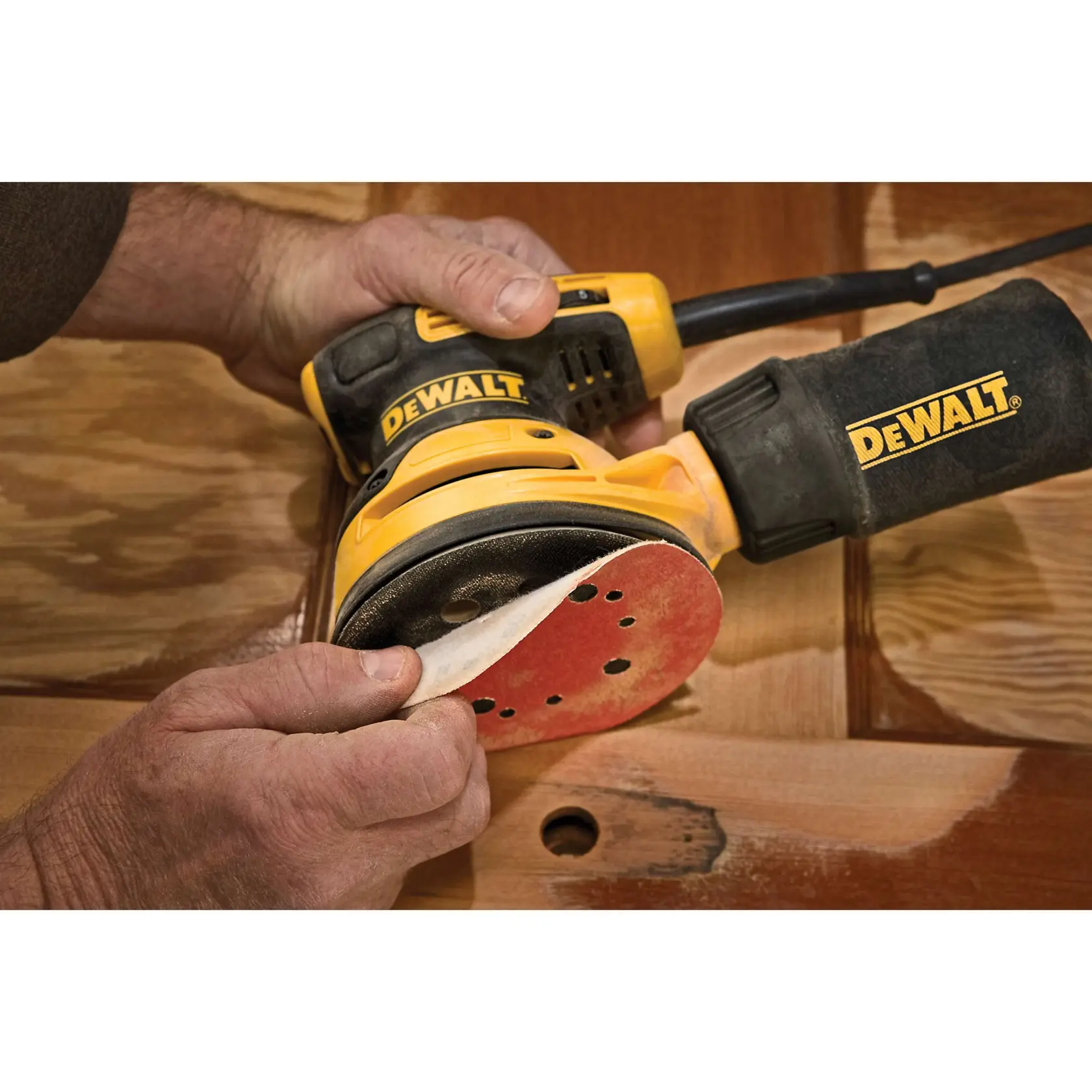 A person applies a sanding disc to a DEWALT electric sander, preparing it for use on a wooden surface.