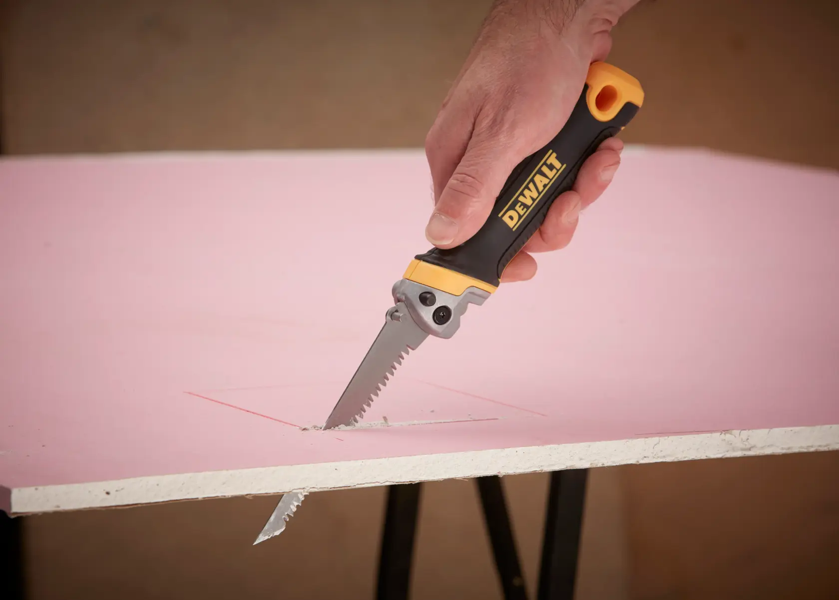 DEWALT folding hand saw with black and yellow bi-material grip. The image labels key features: triple ground teeth, folding mechanism, stainless steel rasp, locking mechanism, and bi-material grip.