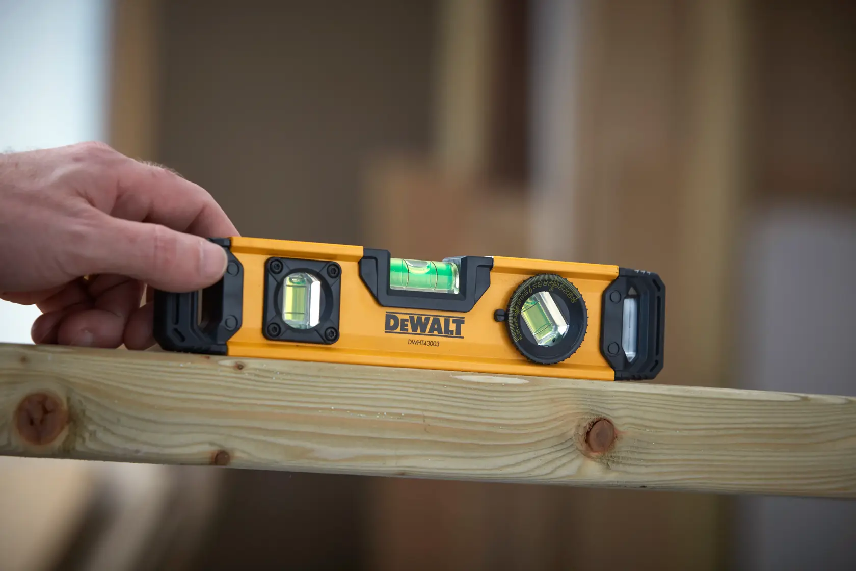 Hand holding a DEWALT DWHT43003 level tool on a wooden beam, used for measuring straightness or angles.