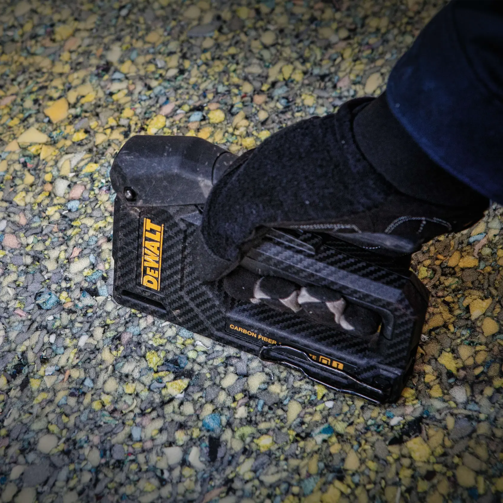 Eine Person benutzt einen DEWALT-Tacker, Modell DWHT80276, um ein Materialblatt an einem Holzrahmen auf einer Baustelle zu befestigen.