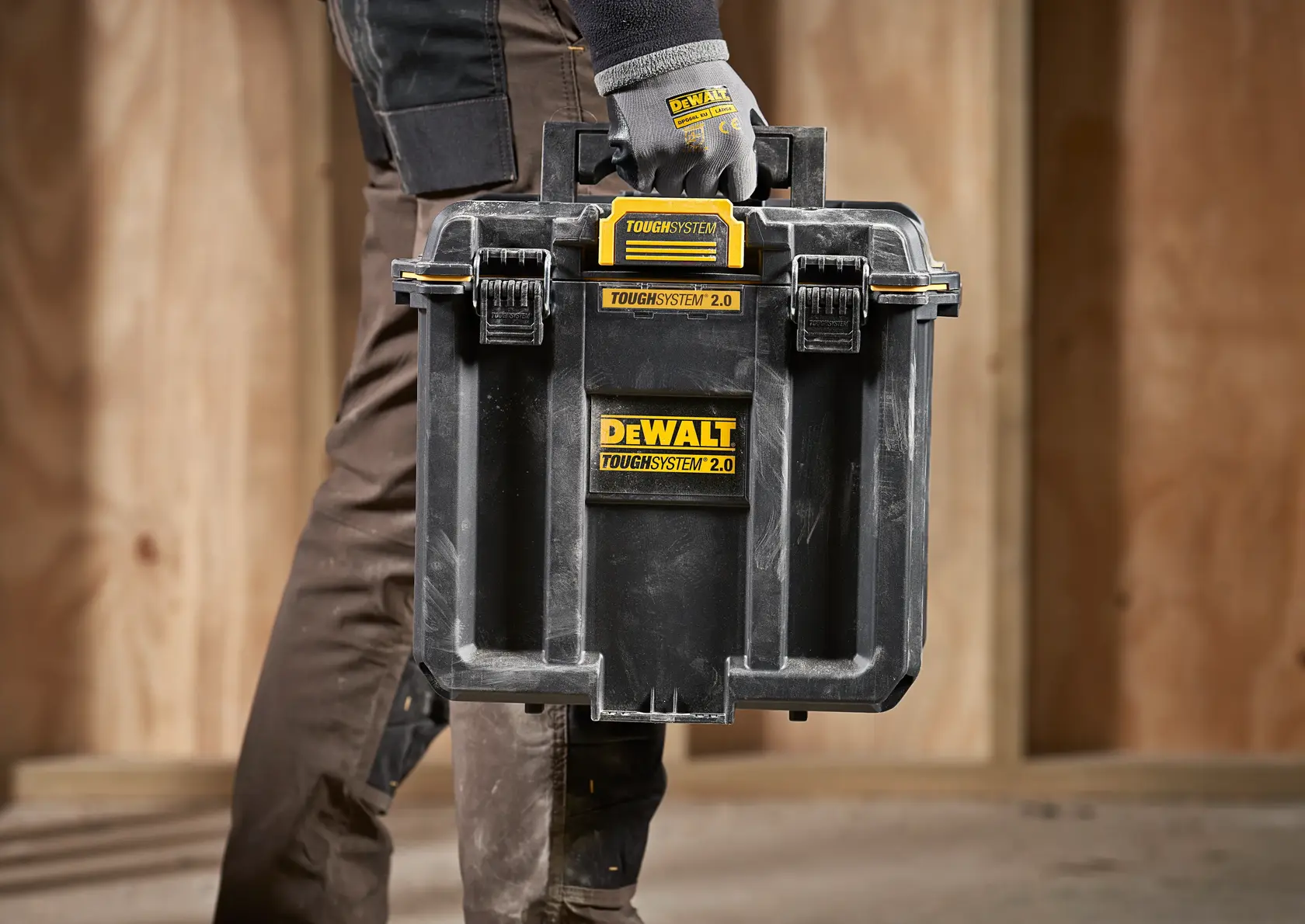 Person carrying a DEWALT ToughSystem 2.0 tool box with gloves at a construction site.