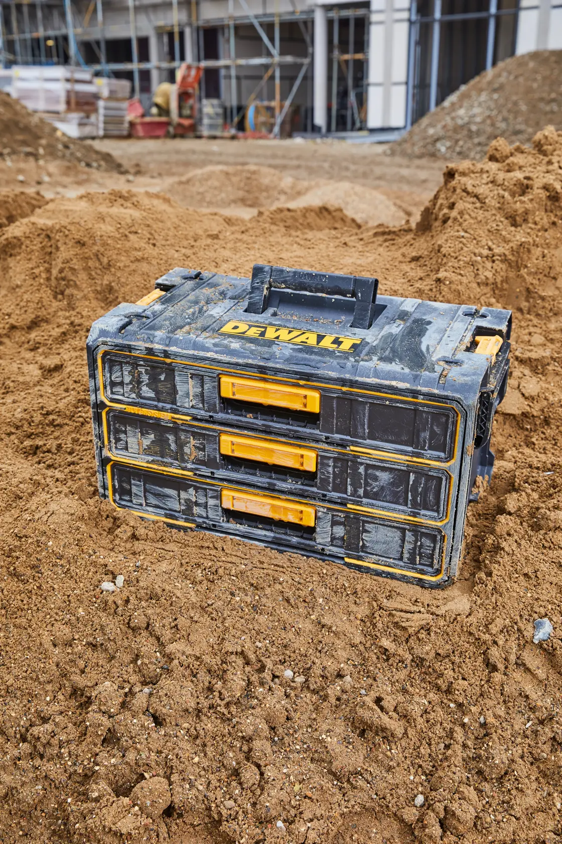 DEWALT three-drawer tool box sitting on a construction site with dirt and building materials in the background.