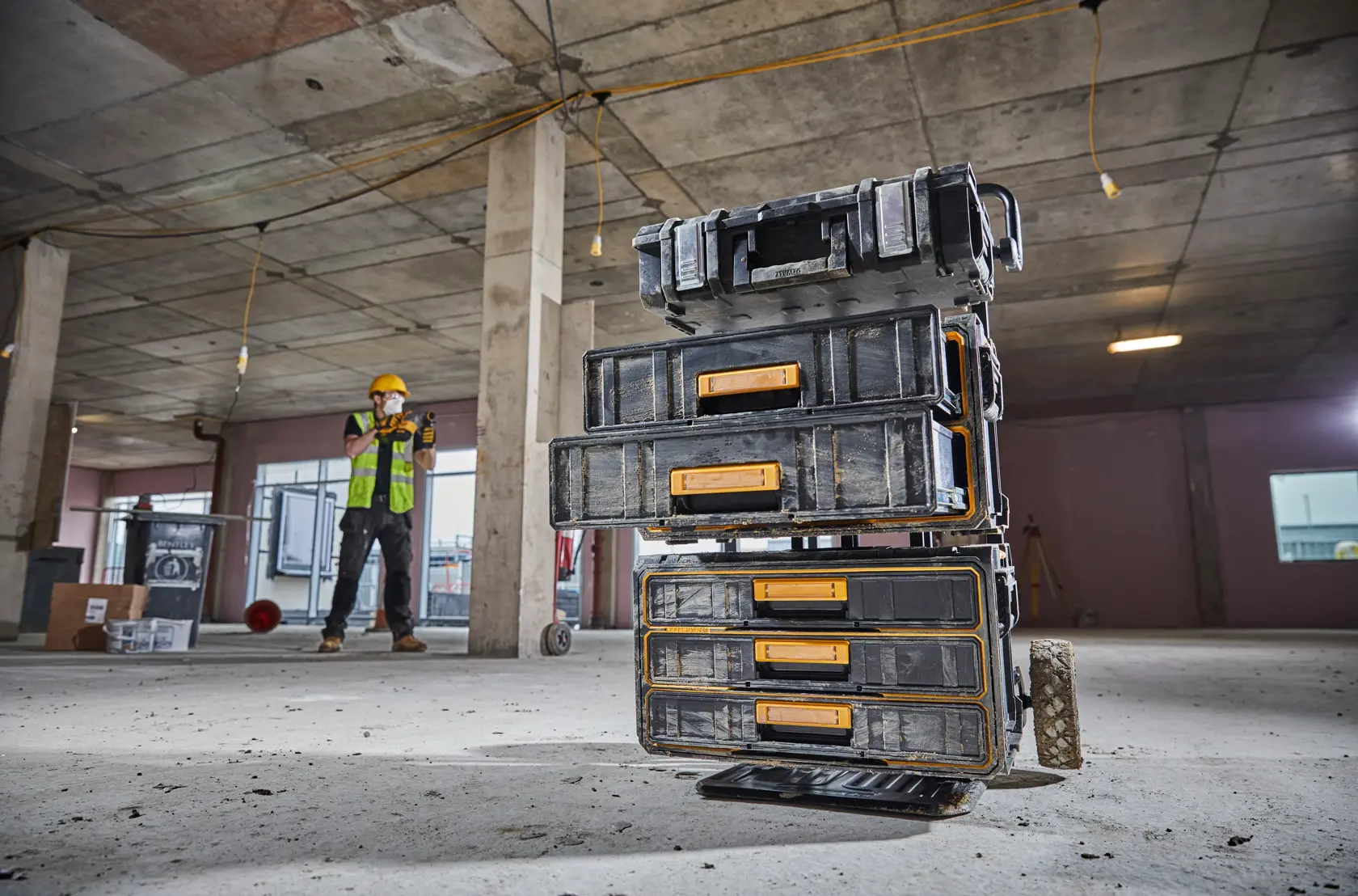 DEWALT DWST1-81055 tool storage boxes stacked on a construction site floor with worker in background.