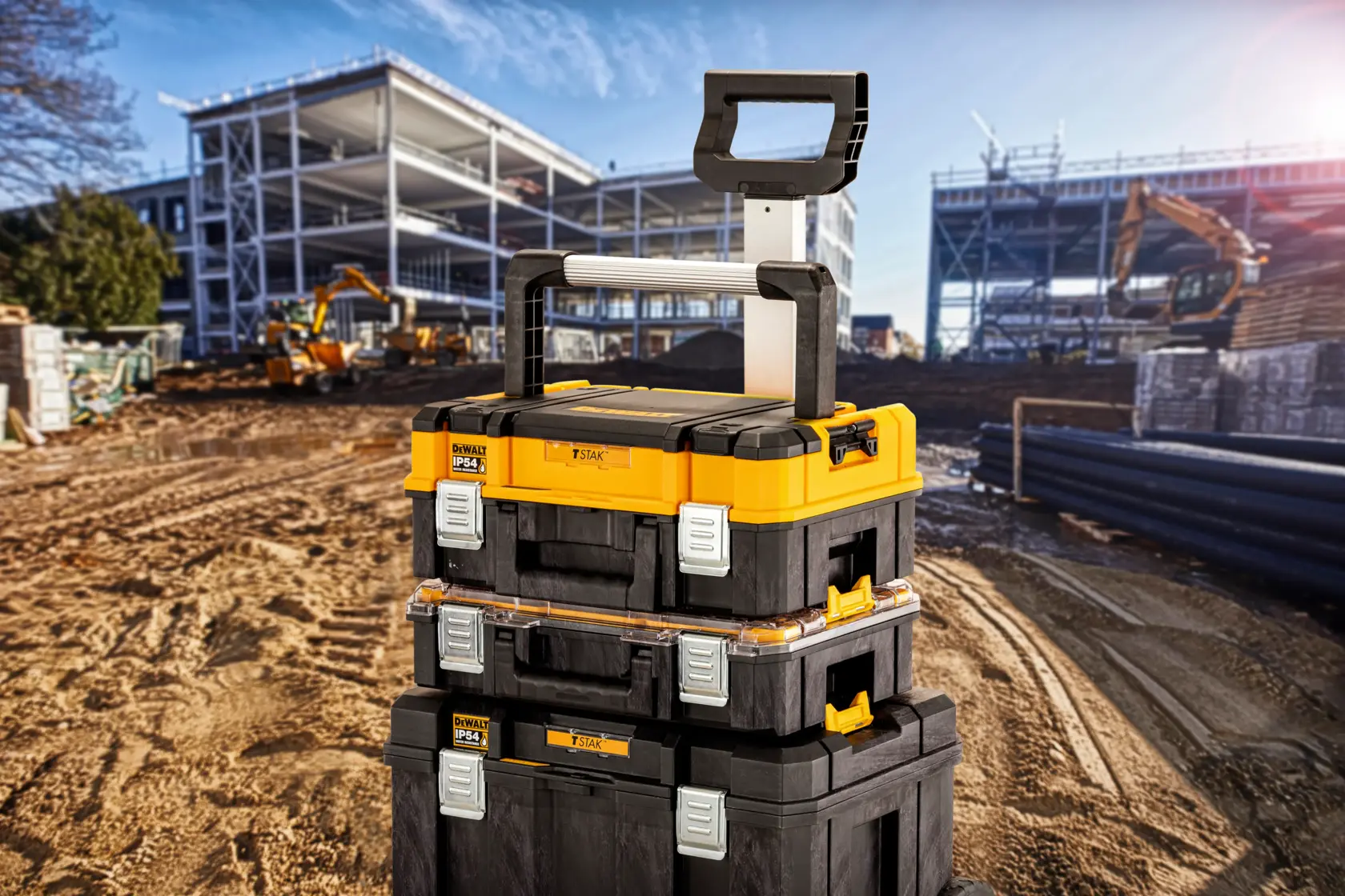 Cajas de herramientas apilables DEWALT con asa en obra, tres cajas frente a estructura de edificio.